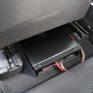 運転席／助手席ともにパワーアンプのサイズは完全には収めきれず、後部座席の足もとスペースにせり出しているのがわかる。